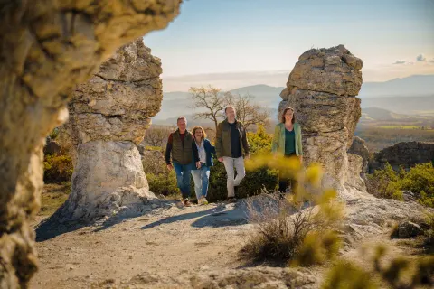 Quatre personnes marchant entre deux rochers sculptés par le vent, paysage de Haute-Provence au soleil couchant