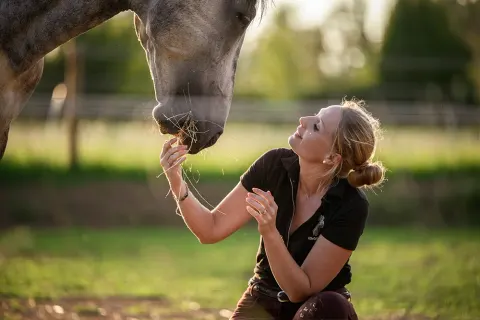 Éleveuse caressant un cheval dans une prairie