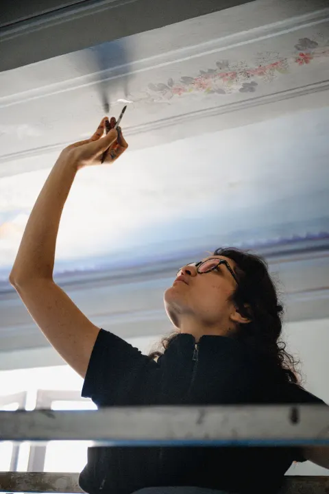 Une artiste peint à la main une frise de fleurs sur un plafond mouluré