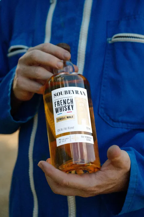 Bouteille de whisky Soubeyran tenue par un agriculteur en bleu de travail