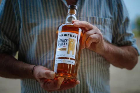 Bouteille de whisky Soubeyran tenue à deux mains devant une chemise rayée